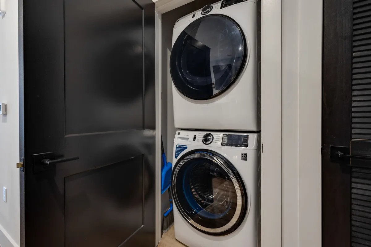 A practical laundry area featuring a stacked washer and dryer against a modern backdrop, with a sleek black door nearby. The space is clean, organized, and clearly dedicated to household chores, emphasizing convenience and efficiency for guests.