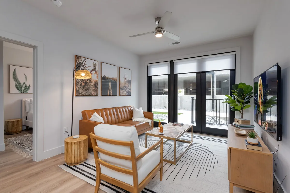 A cozy living room with a brown leather sofa, wooden side table, framed artwork, and large windows. The room feels inviting and comfortable, offering a perfect nook for relaxing or sleeping on the twin futon.