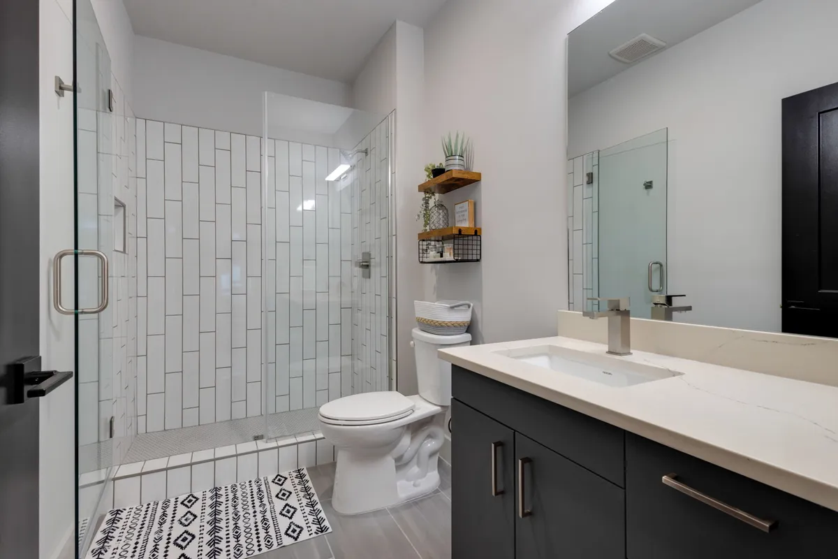 A modern bathroom featuring a glass shower enclosure, sleek sink and countertop, and decorative shelving with plants. The space is bright, clean, and spa-inspired, inviting relaxation and self-care routines.