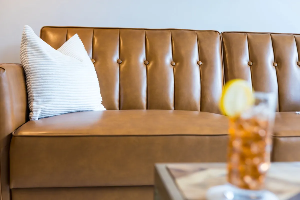A chic communal lounge with a tan leather sofa, striped pillow, and a glass of drink on the side table—exuding comfort and a welcoming environment for socializing or relaxing.