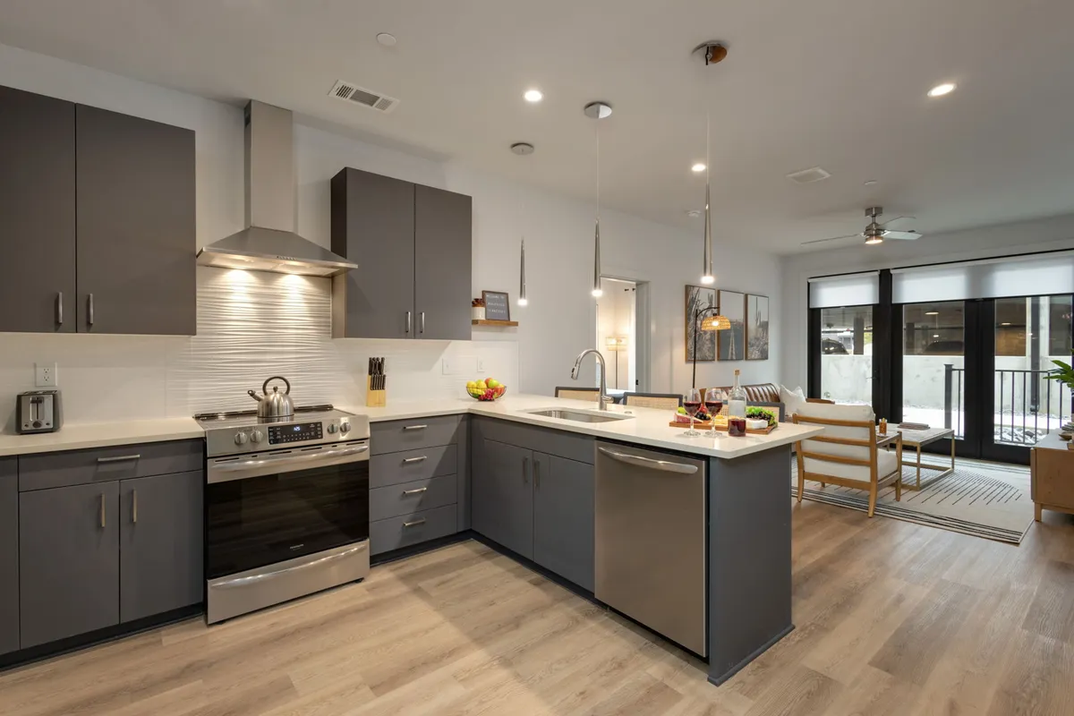 A contemporary kitchen scene with modern cabinetry, stainless steel appliances, a spacious kitchen island with a sink, and an adjacent dining area visible through the open layout. The design fosters a seamless flow between cooking, dining, and socializing.