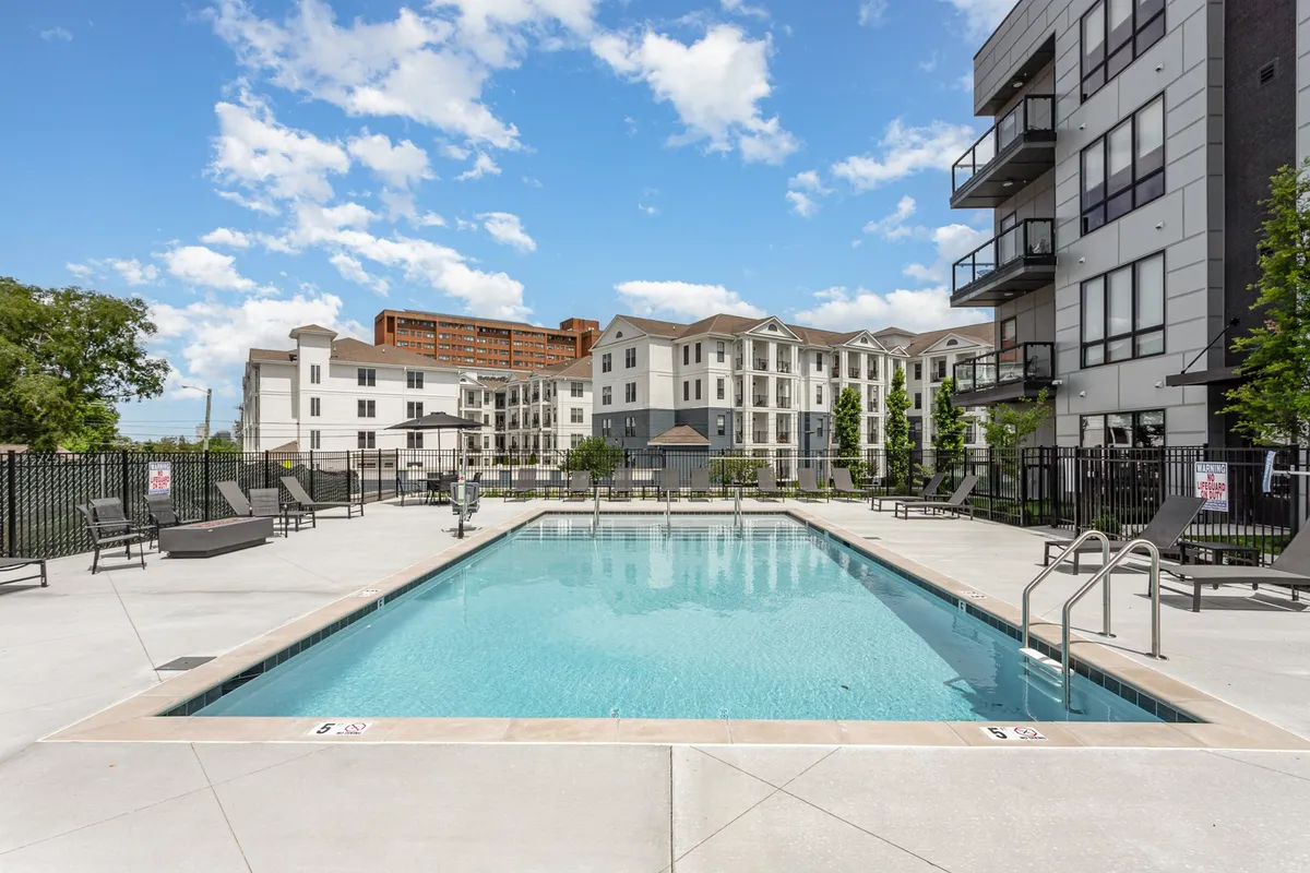 A modern outdoor pool area at the Savanna property, surrounded by lush trees and stylish apartment buildings. Sun loungers beckon for relaxation, and the inviting water reflects the city’s skyline at sunset.
